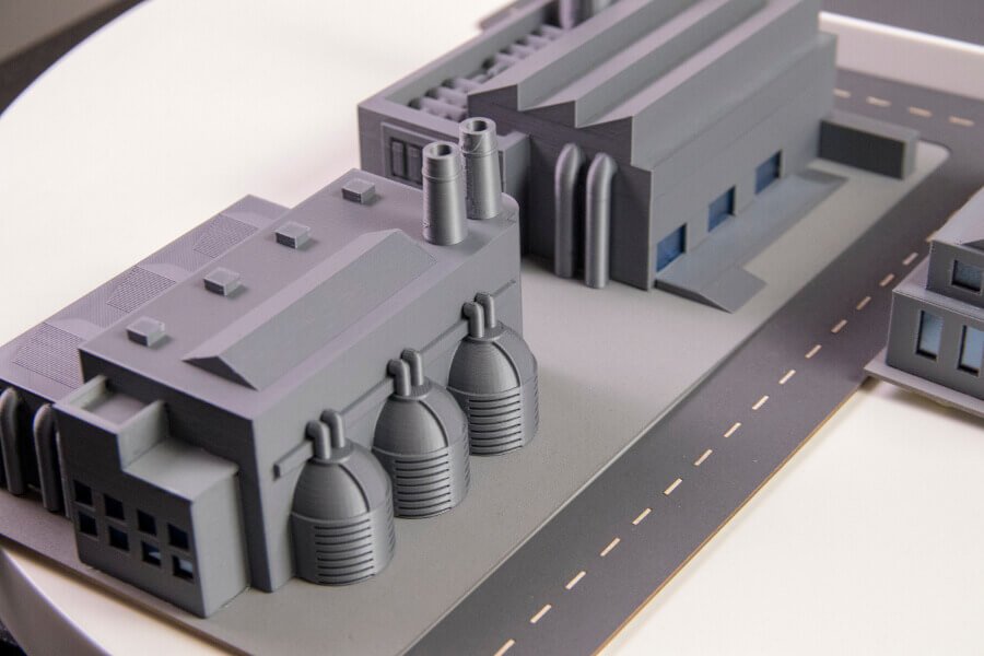 A grey 3D printed scale model of an industrial plant showing tanks, chimneys and roads on a base plate