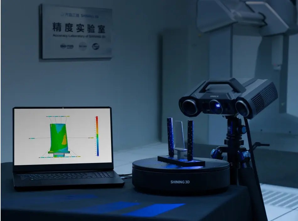 Structured-light 3D scanner over a turntable showing a colour deviation map on screen in an accuracy laboratory