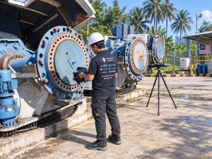 Engineer with a handheld 3D scanner and a tripod-mounted optical tracker measuring large industrial machinery outdoors