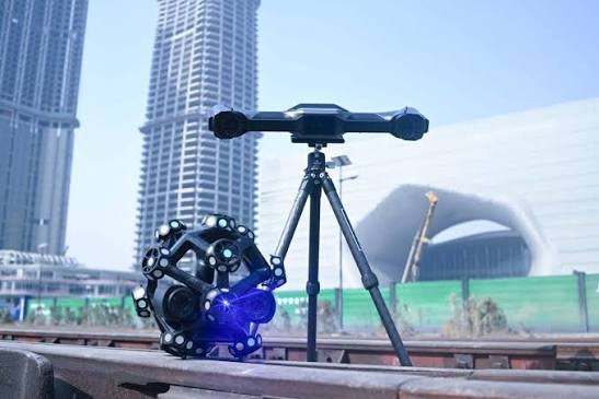 Optical tracker on a tripod beside a wireless marker-covered 3D scanner outdoors in a city