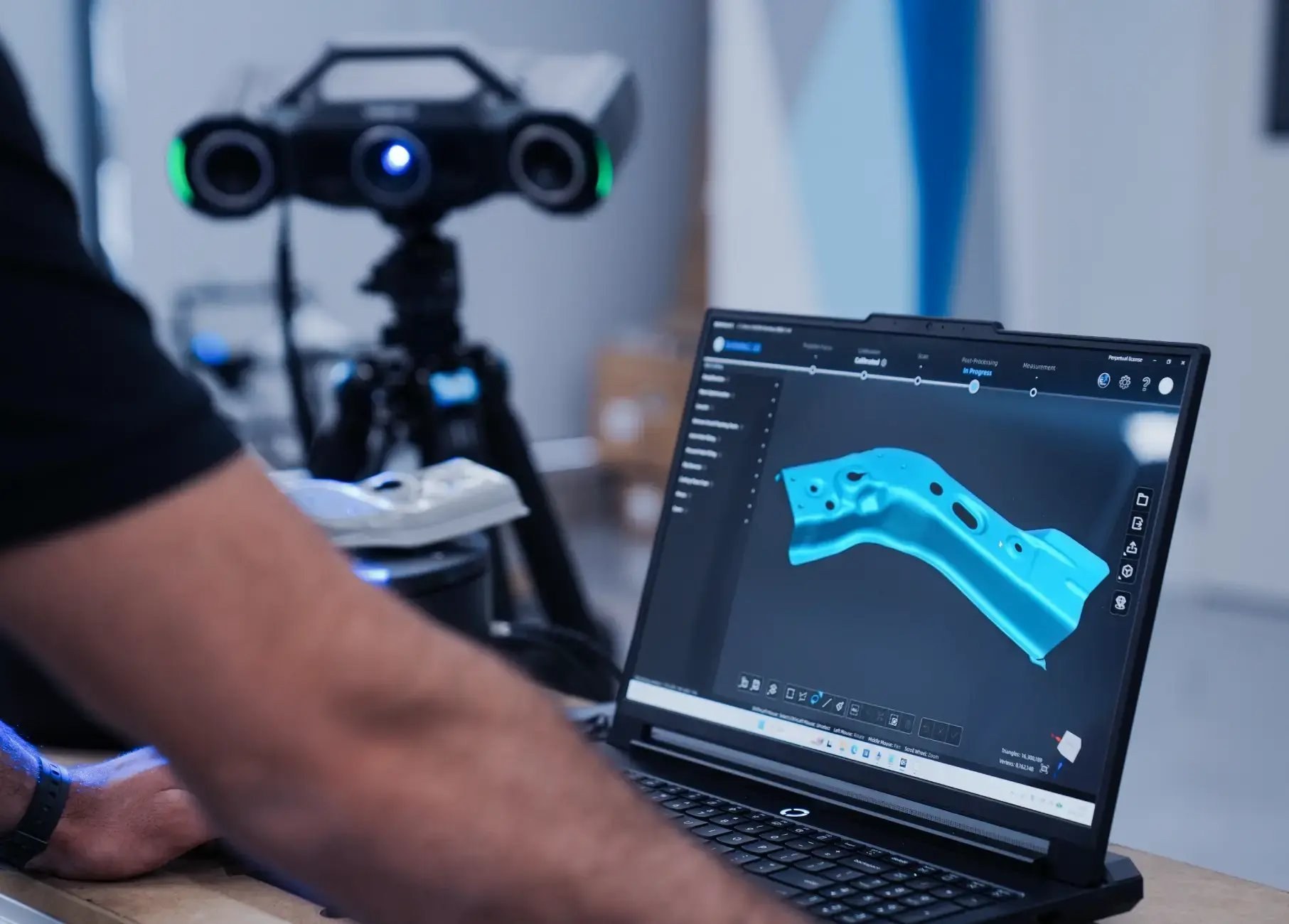 Portable 3D scanner on a tripod beside a laptop displaying captured scan data