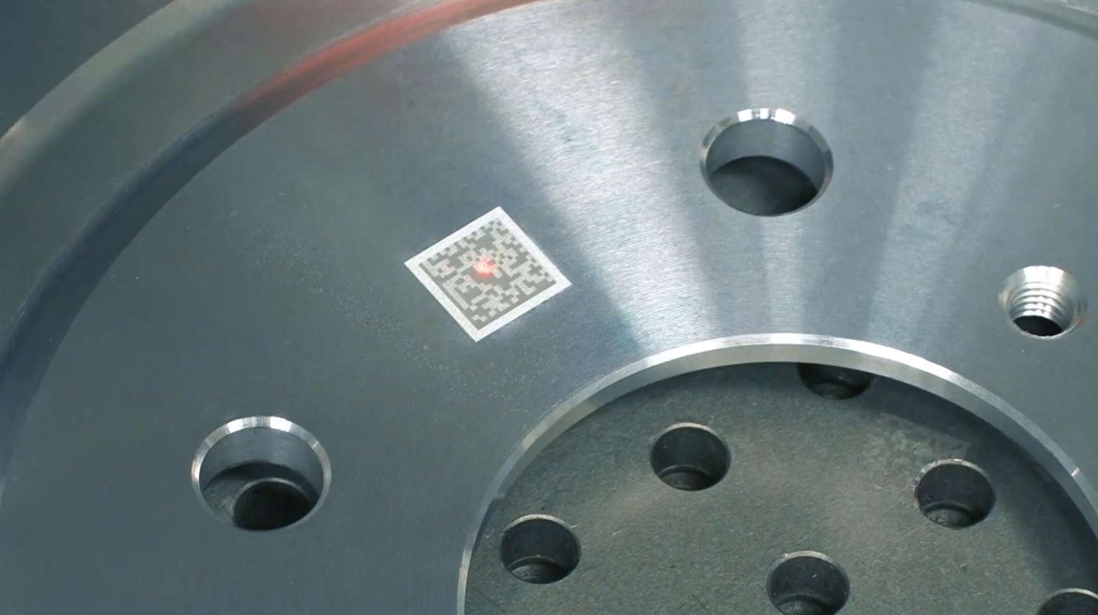 Close-up of a Data Matrix code being laser marked onto a machined steel flange, showing the marking point and the finished cells