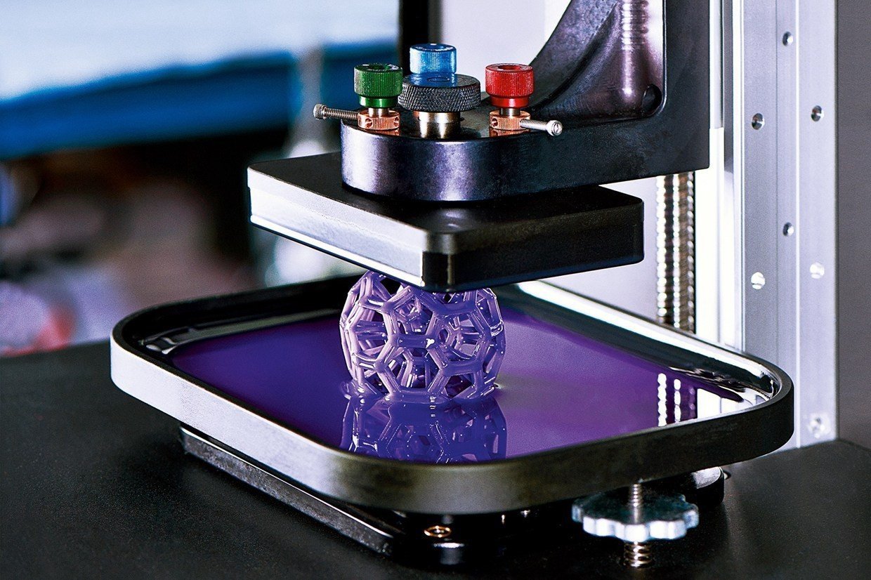 A DLP resin 3D printer with its build platform lowering a lattice part into a vat of violet photopolymer resin