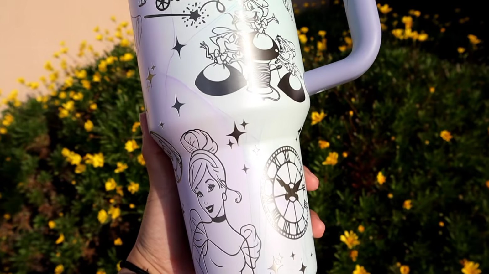 Close-up of a finished engraved tumbler with a black line-art princess and carriage design, held outdoors