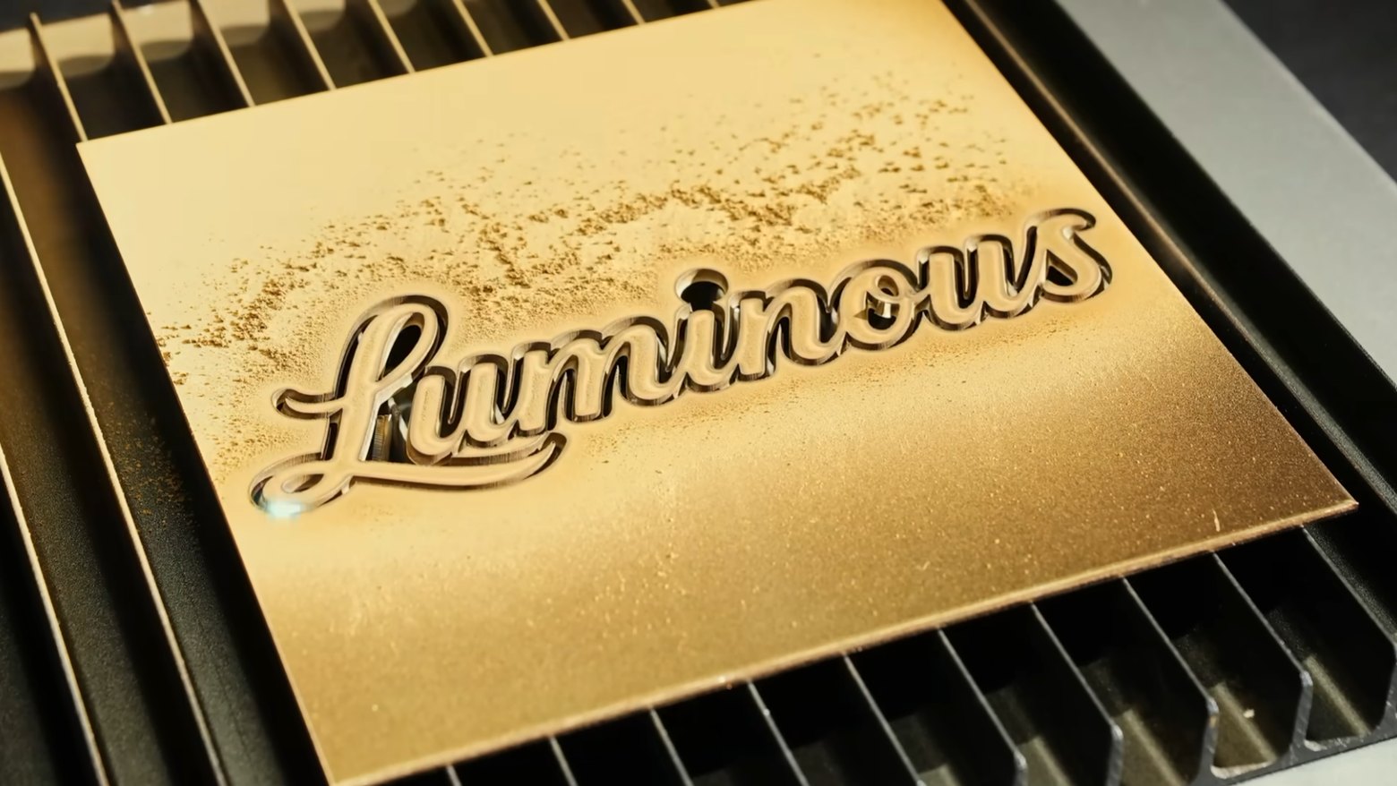 Close-up of a script logo cut clean through a gold metal sheet on a fiber laser bed
