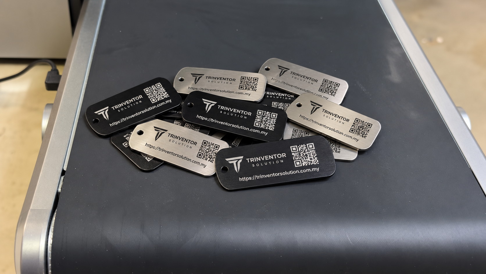 Batch of engraved steel and black aluminium QR code tags reading Trinventor Solution