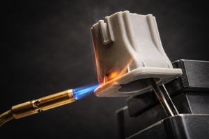 A blowtorch flame applied to a flame-retardant 3D printed part during a burn test