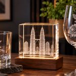 A frosted XTOOL logo on a whisky tumbler beside a crystal block with the Kuala Lumpur skyline engraved inside it