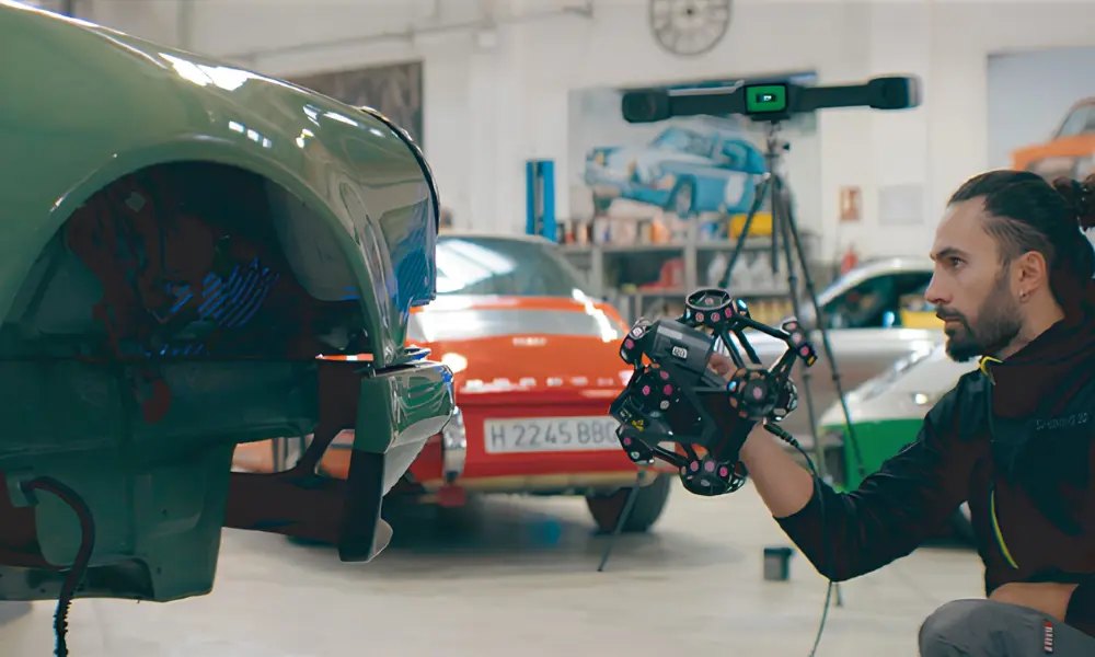 An operator using a handheld Shining 3D scanner with tracking markers to capture a car body panel in a workshop