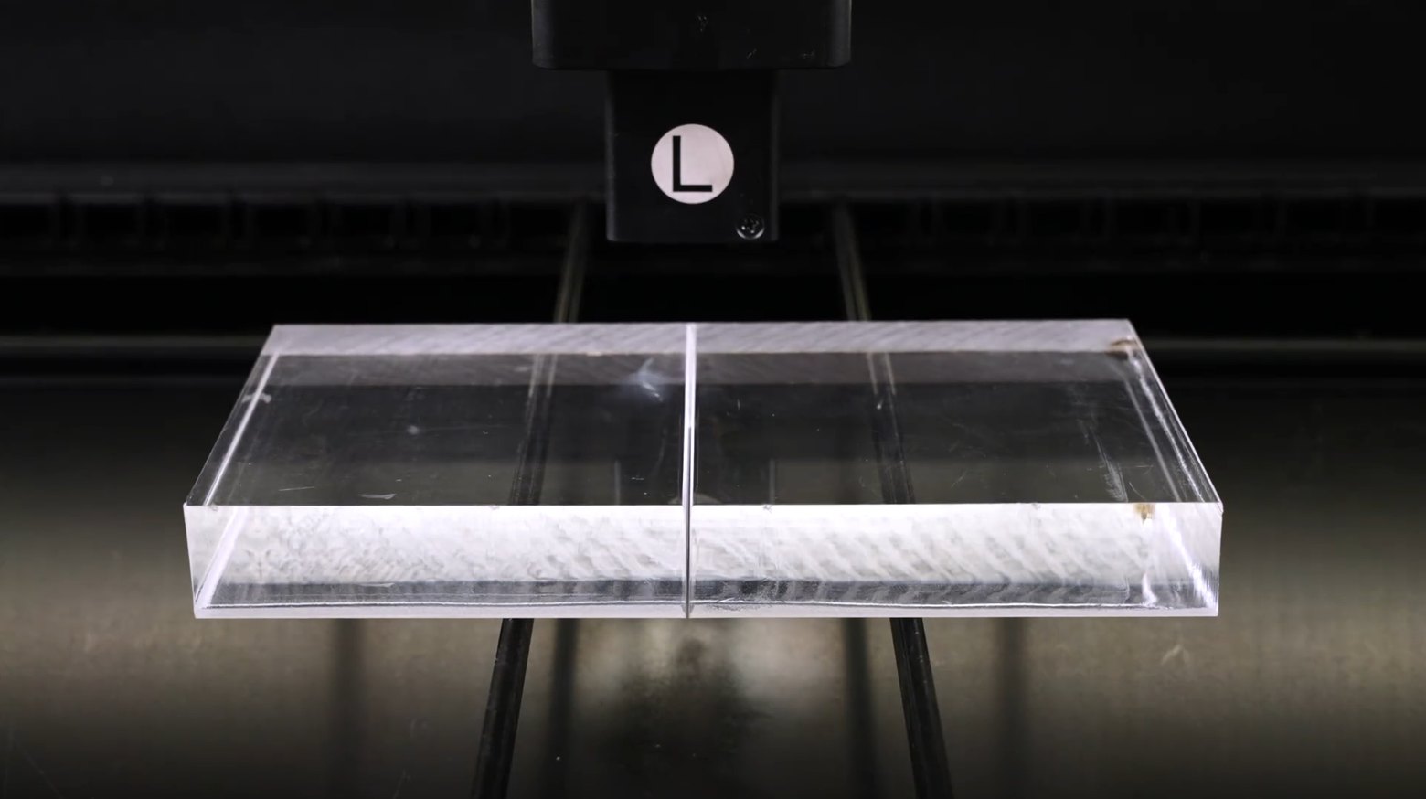 A thick clear acrylic block on the laser bed with the cut line and frosted edge visible