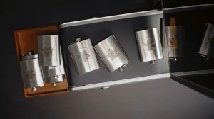 Laser-engraved stainless steel hip flasks with mandala logos, some marked in colour, displayed in a presentation box
