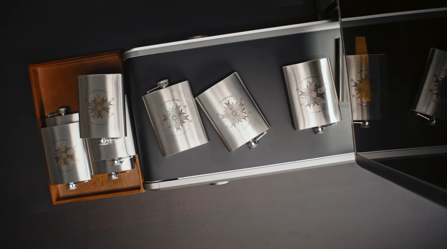 Laser-engraved stainless steel hip flasks with mandala logos, some marked in colour, displayed in a presentation box