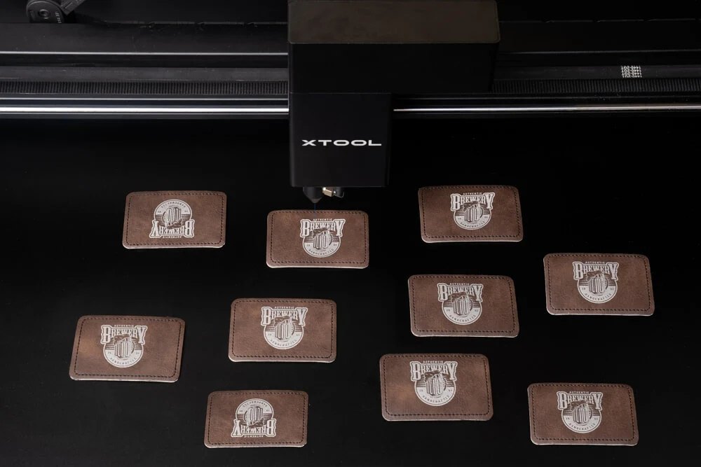 A laser engraving custom logos onto brown leather patches on the machine bed