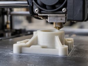 A 3D printer nozzle laying down layers of natural nylon to build a flanged bracket