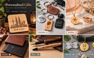 A range of personalised gifts — an engraved Kuala Lumpur skyline plaque, leather and wooden keyrings, a gold hibiscus pendant and ring, engraved leather wallets, engraved wooden pens, and engraved pet tags