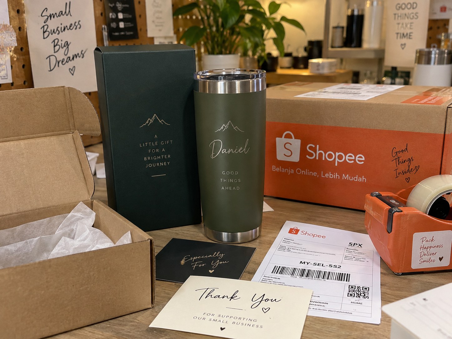 A personalised tumbler and gift box beside an open Shopee shipping carton, packing tape and a thank-you card