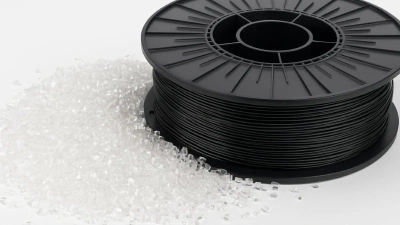 PETG filament wound on a spool beside a pile of translucent raw resin pellets before extrusion