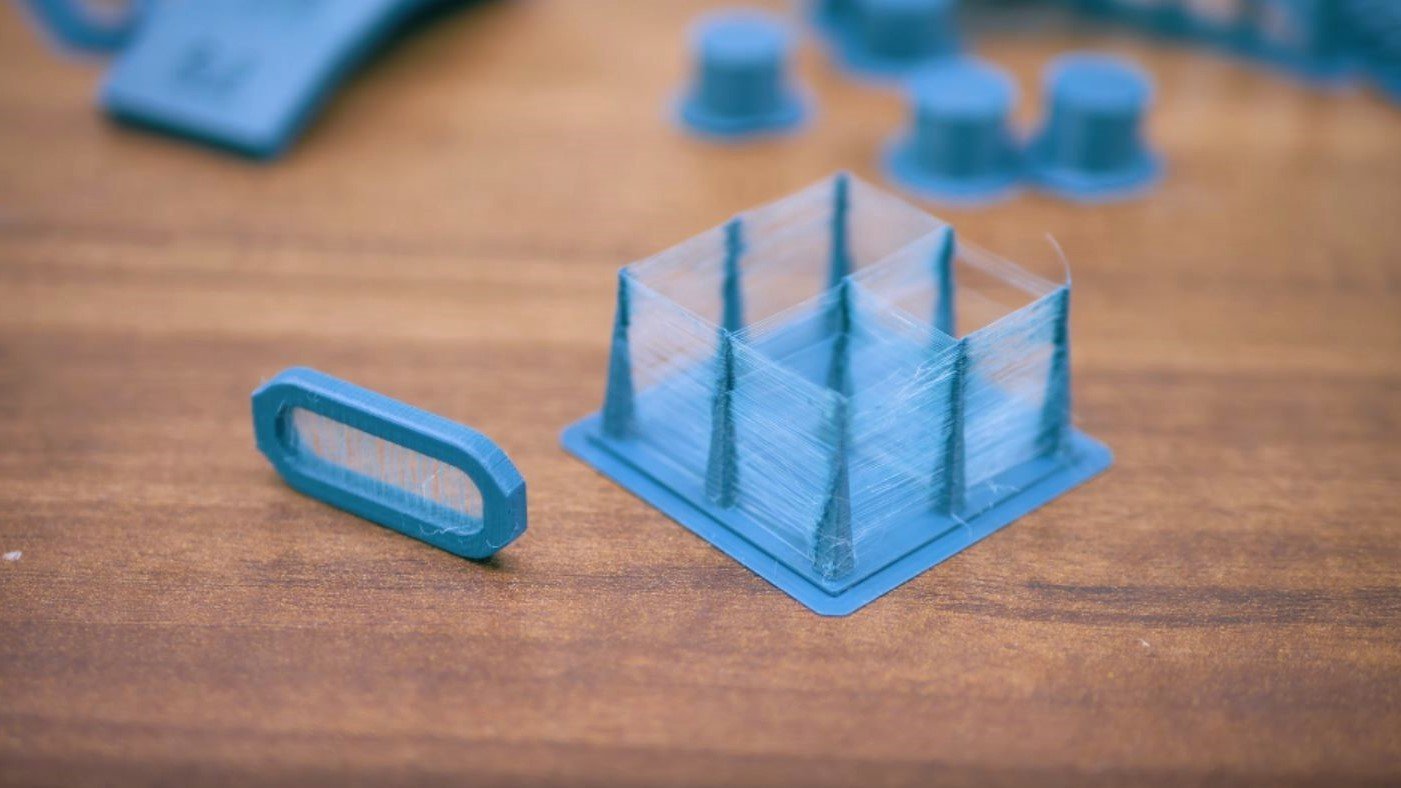 Blue PETG test print covered in fine stringing wisps across the gaps between its walls