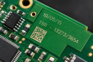 Close-up of a green printed circuit board with a laser-marked date, batch number and 2D data matrix code