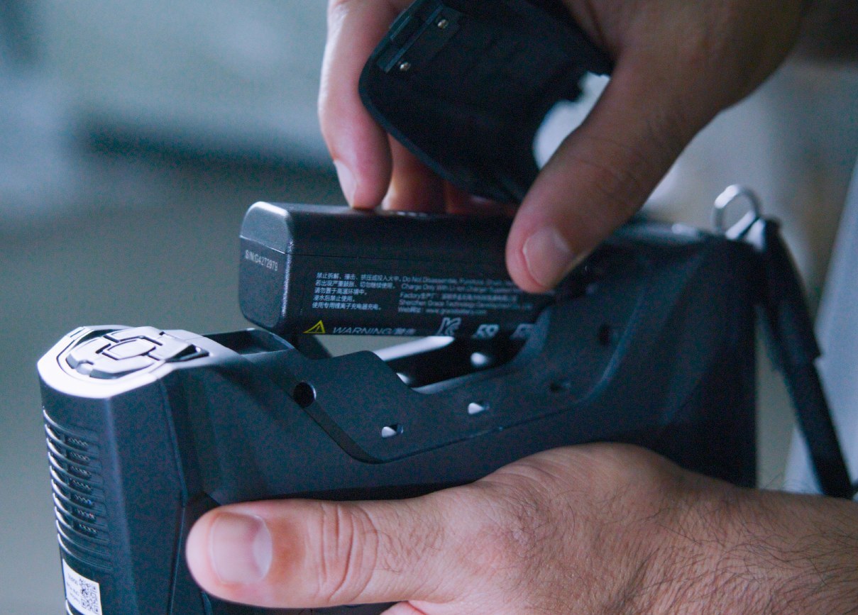 Hands holding a 3D scanner over a component on a bench