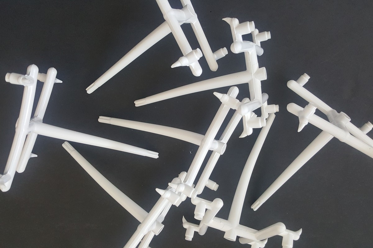 A batch of white 3D printed parts with their support structures, laid out on a dark surface