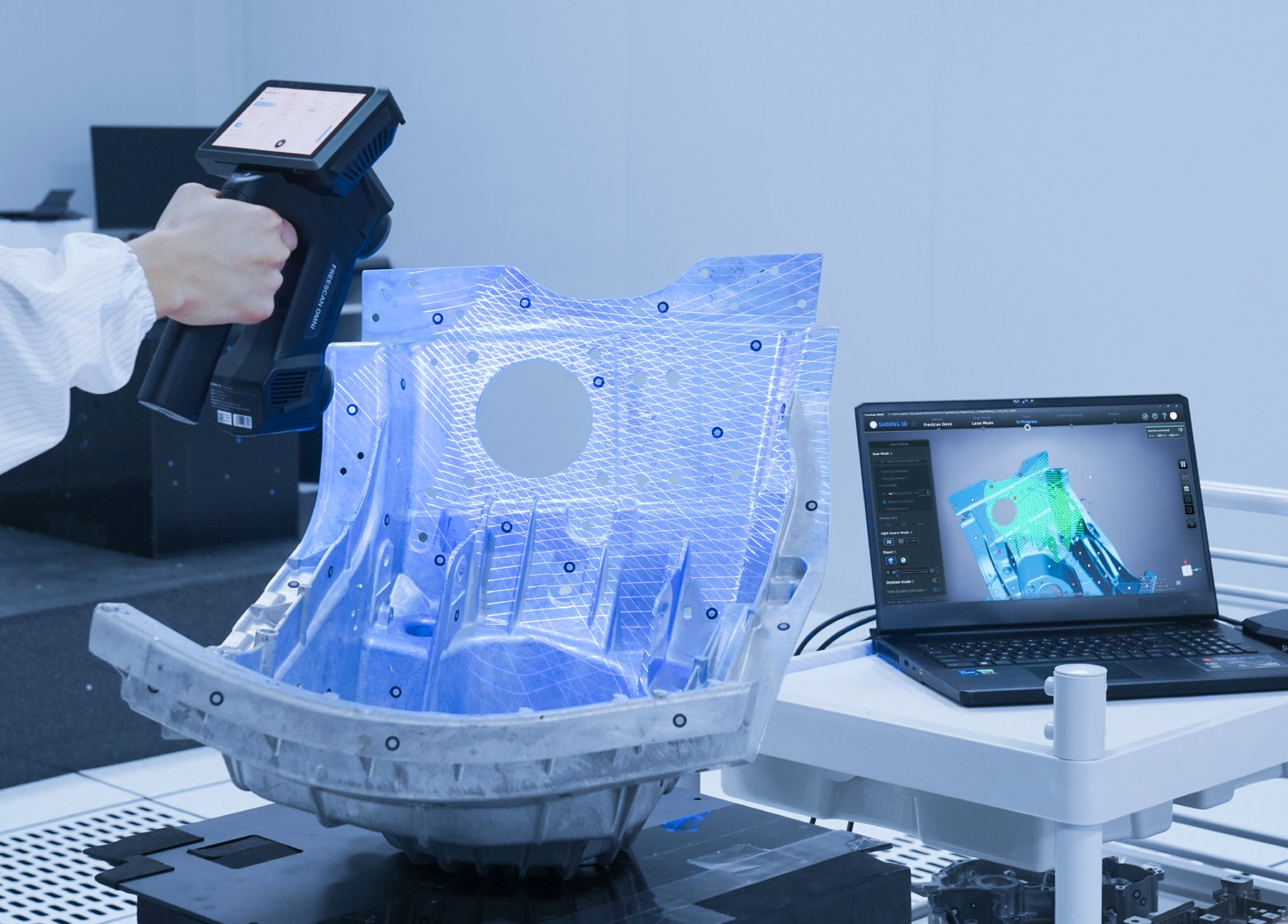 A Shining 3D FreeScan handheld scanner projecting laser lines across a car body panel with targets, scan on screen