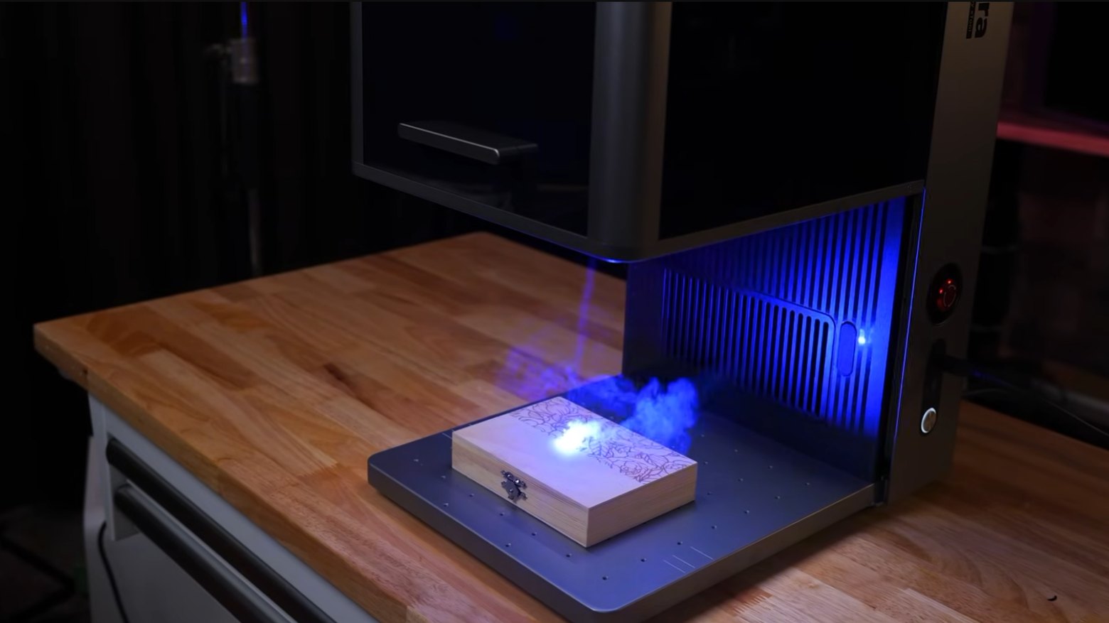 The xTool F2 Ultra fiber laser engraving a floral pattern onto a wooden gift box, with the blue laser beam and smoke visible in the enclosure