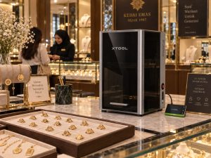 The xTool F2 Ultra on a jewellery shop counter beside trays of gold rings and custom engraving signboards